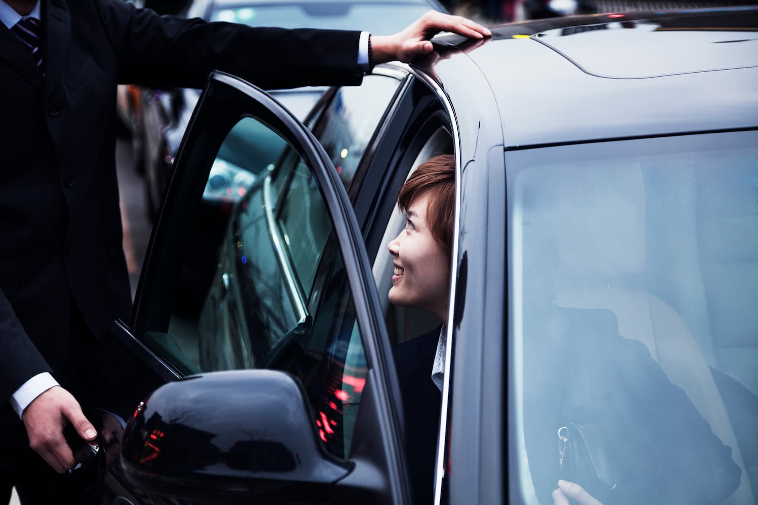 Chauffeur opening the rear door of a car for a passenger